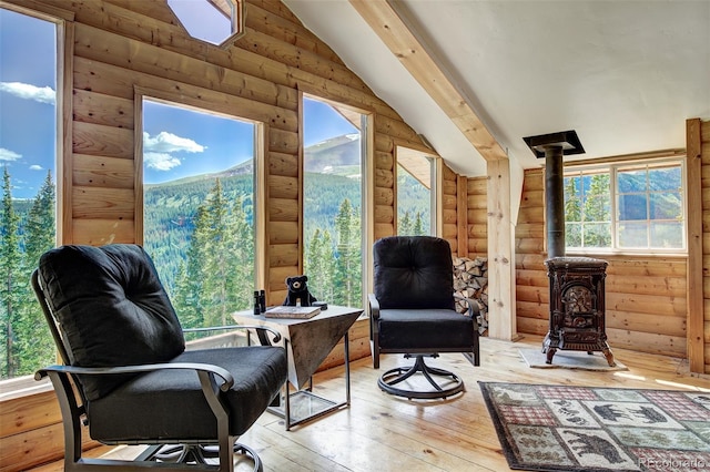 sitting room featuring light hardwood / wood-style floors, a wood stove, vaulted ceiling with skylight, and rustic walls