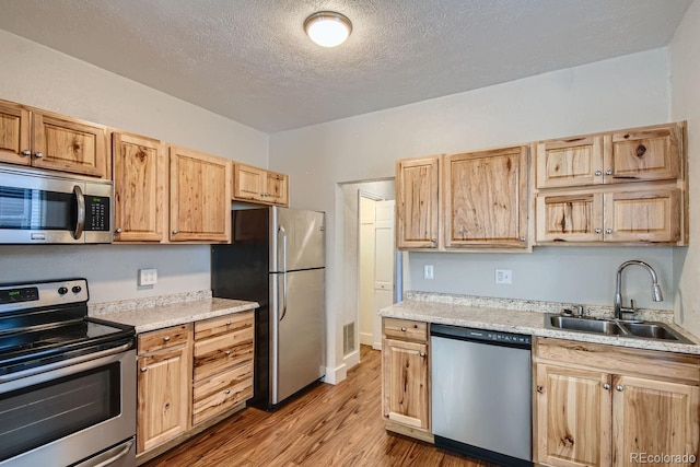 kitchen with light brown cabinets, light hardwood / wood-style floors, stainless steel appliances, and sink