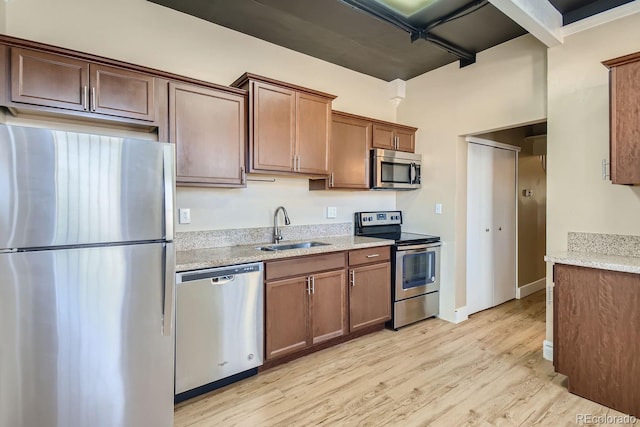 kitchen featuring appliances with stainless steel finishes, sink, light stone counters, and light hardwood / wood-style flooring