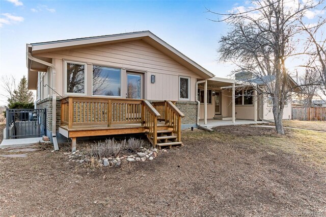 back of property with a wooden deck, a patio, brick siding, and fence