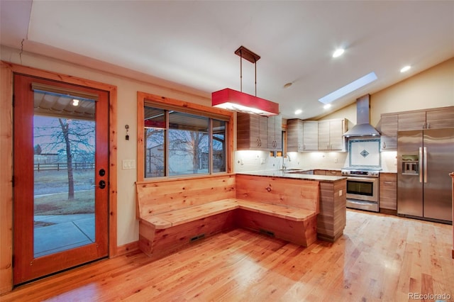 kitchen with a sink, stainless steel appliances, a peninsula, wall chimney exhaust hood, and lofted ceiling