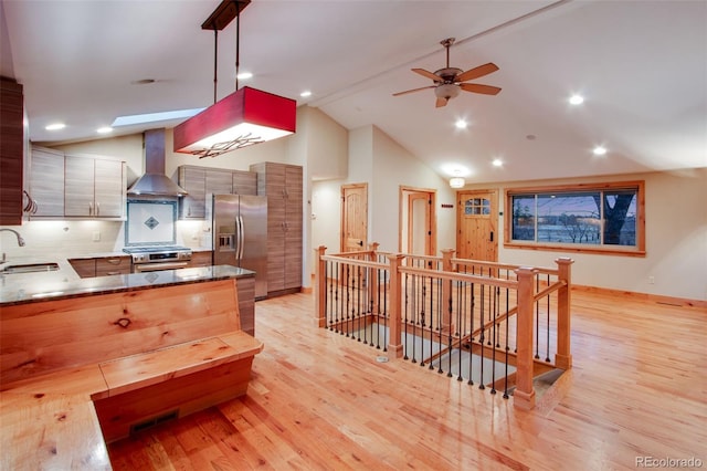 kitchen featuring light wood finished floors, stainless steel appliances, hanging light fixtures, a sink, and wall chimney range hood