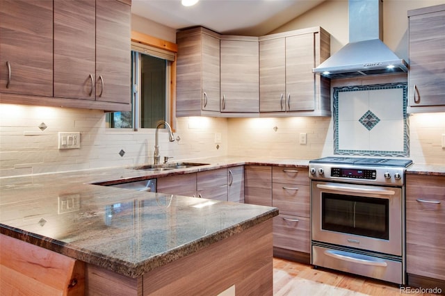 kitchen featuring a sink, a peninsula, wall chimney exhaust hood, light stone countertops, and stainless steel range with gas stovetop