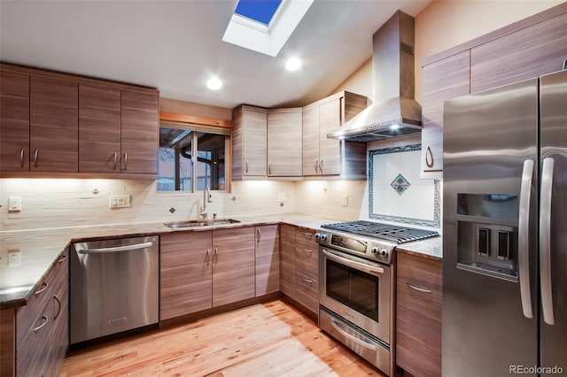 kitchen featuring decorative backsplash, light wood-style floors, stainless steel appliances, wall chimney exhaust hood, and a sink