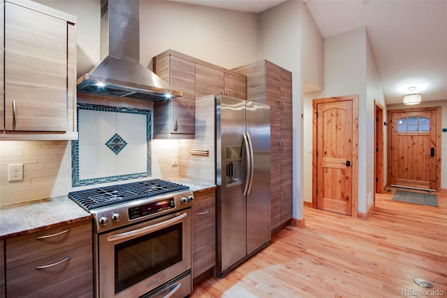 kitchen featuring wall chimney range hood, light wood-style flooring, light stone countertops, and stainless steel appliances