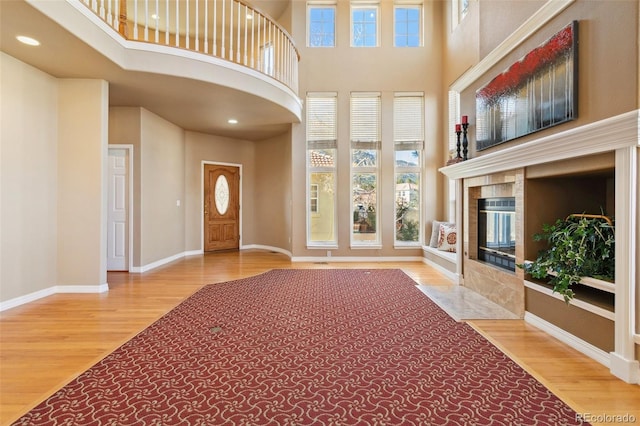 foyer entrance with a fireplace, a towering ceiling, wood-type flooring, and plenty of natural light