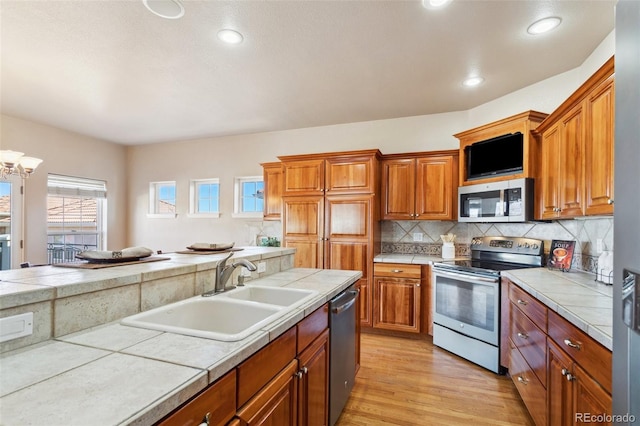 kitchen with tasteful backsplash, sink, tile counters, light hardwood / wood-style floors, and stainless steel appliances