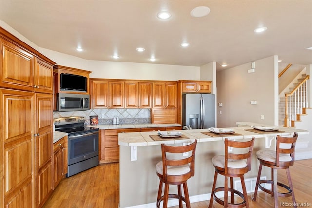 kitchen with a breakfast bar, tasteful backsplash, light wood-type flooring, appliances with stainless steel finishes, and a kitchen island