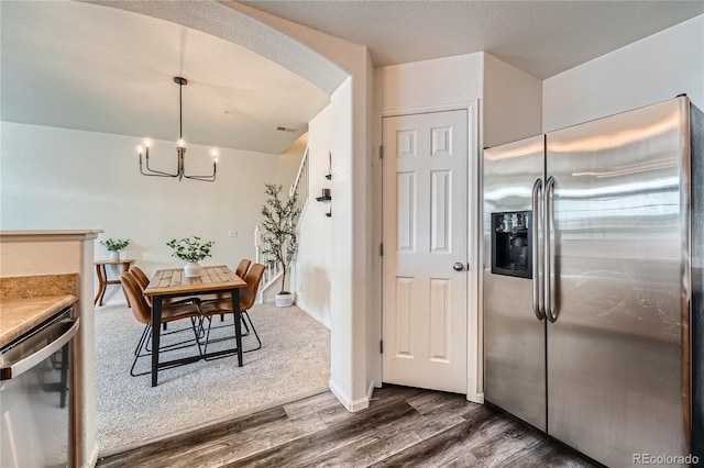 kitchen with appliances with stainless steel finishes, an inviting chandelier, hanging light fixtures, a textured ceiling, and dark hardwood / wood-style flooring