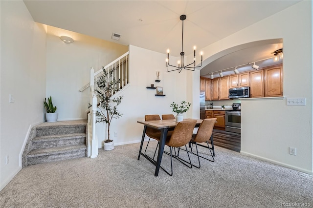 carpeted dining room featuring rail lighting and a chandelier