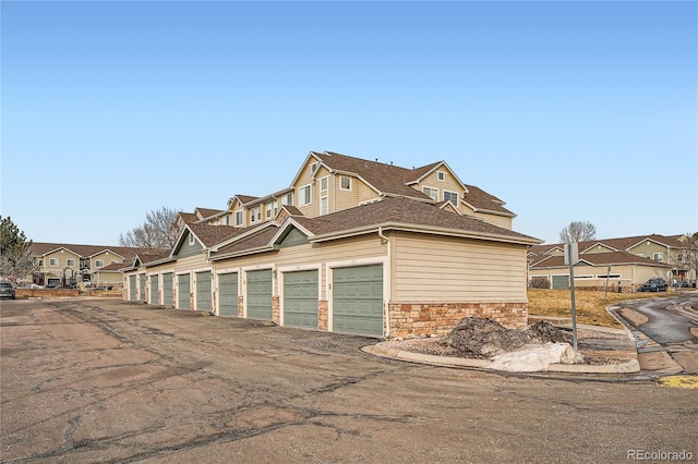 view of home's exterior with a residential view, stone siding, roof with shingles, and community garages