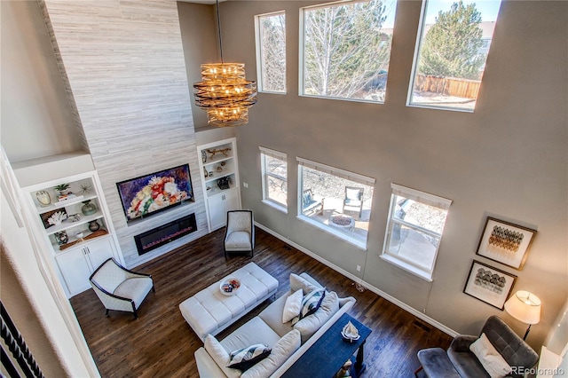 living area featuring a chandelier, a tile fireplace, a high ceiling, wood finished floors, and built in features