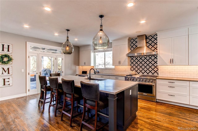 kitchen featuring dark wood finished floors, a sink, an island with sink, high end stove, and wall chimney exhaust hood