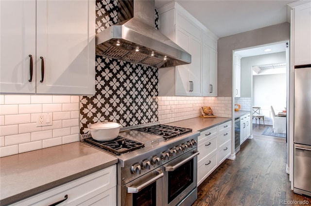 kitchen with dark wood-style flooring, stainless steel appliances, decorative backsplash, white cabinetry, and wall chimney exhaust hood