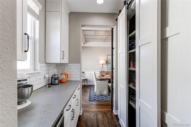 kitchen with dark wood-style flooring, a wainscoted wall, light countertops, a barn door, and white cabinets