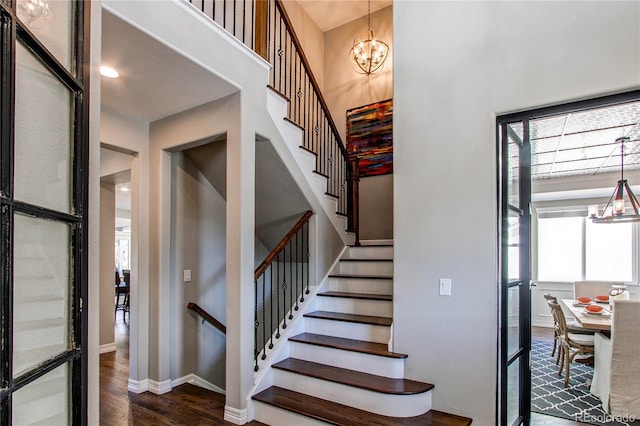 stairs featuring wood finished floors, baseboards, a high ceiling, and an inviting chandelier