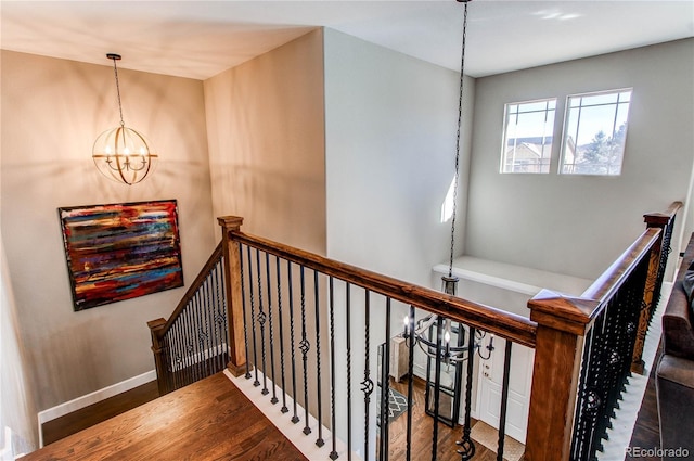 stairway with a chandelier, wood finished floors, and baseboards