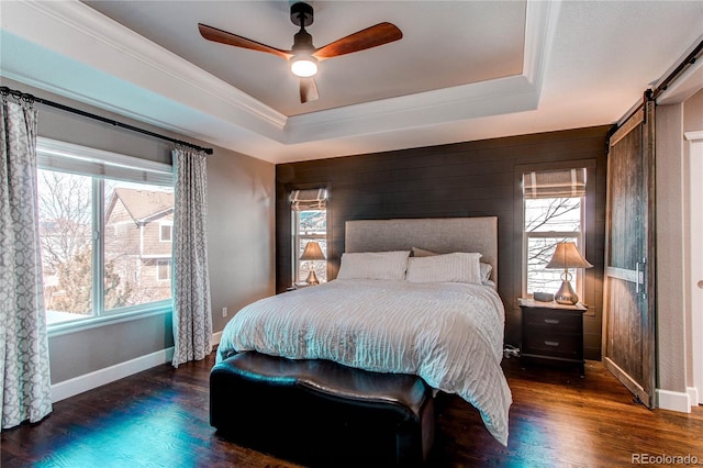 bedroom with wood finished floors, a barn door, and a raised ceiling