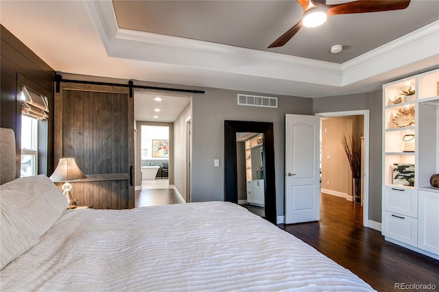 bedroom with dark wood-style floors, a raised ceiling, visible vents, a barn door, and ornamental molding