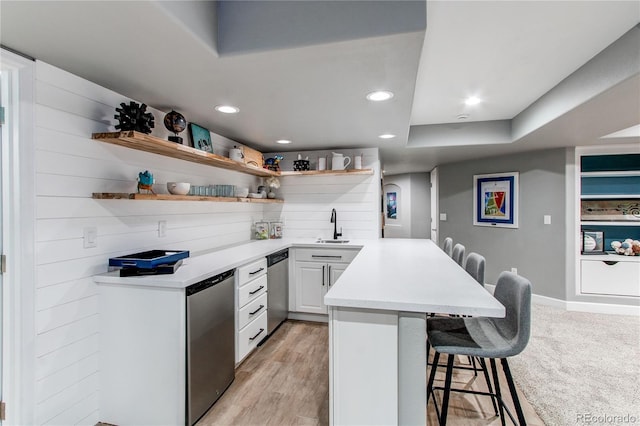 kitchen featuring a peninsula, a sink, a kitchen breakfast bar, stainless steel dishwasher, and open shelves