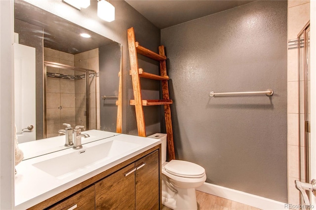 bathroom with toilet, a shower stall, vanity, wood finished floors, and baseboards