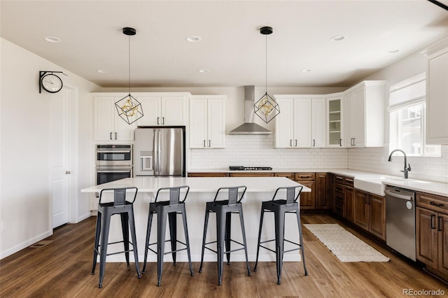 5840 Longs Peak St, Brighton, CO 80601 - kitchen with appliances with stainless steel finishes, wall chimney range hood, dark wood-type flooring, a kitchen breakfast bar, and recessed lighting