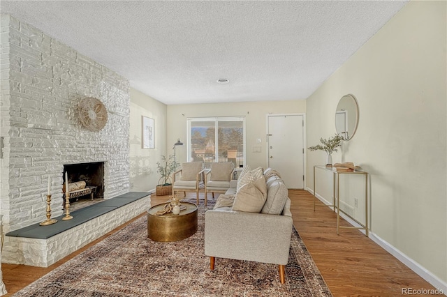 living room with a stone fireplace, hardwood / wood-style floors, and a textured ceiling