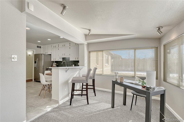 kitchen with a breakfast bar area, white cabinetry, backsplash, stainless steel refrigerator with ice dispenser, and kitchen peninsula