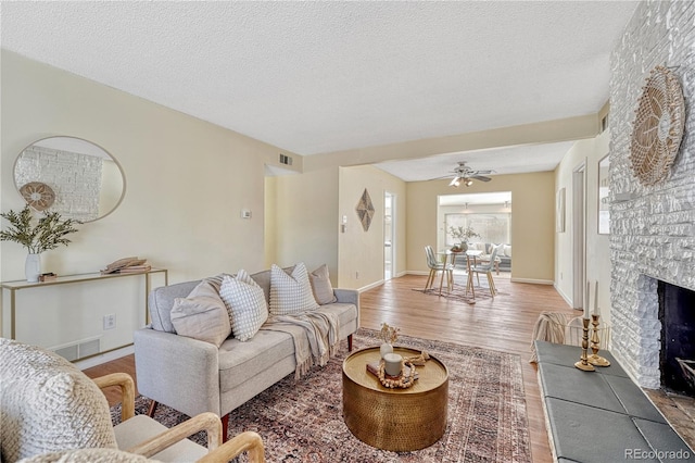 living room featuring ceiling fan, hardwood / wood-style flooring, a stone fireplace, and a textured ceiling