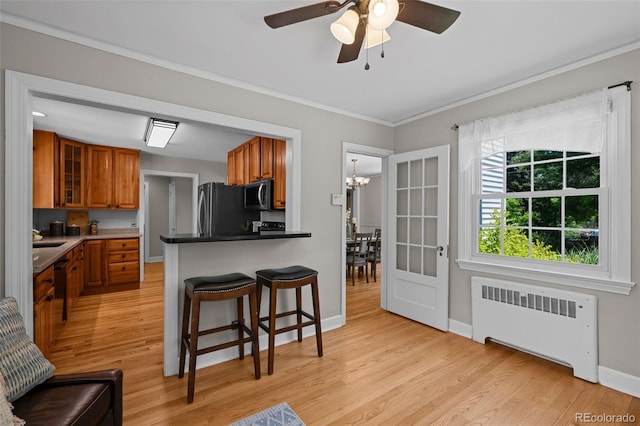 1033 Estes St, Lakewood, CO 80215 - kitchen featuring radiator heating unit, stainless steel microwave, brown cabinetry, a kitchen breakfast bar, and light wood-type flooring