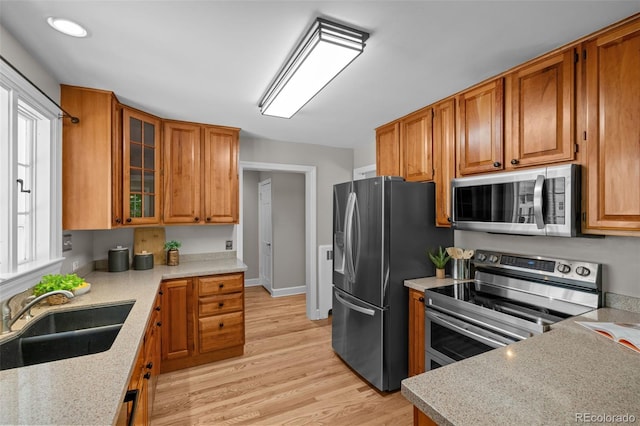 1033 Estes St, Lakewood, CO 80215 - kitchen with stainless steel appliances, brown cabinets, light wood-style floors, and glass insert cabinets