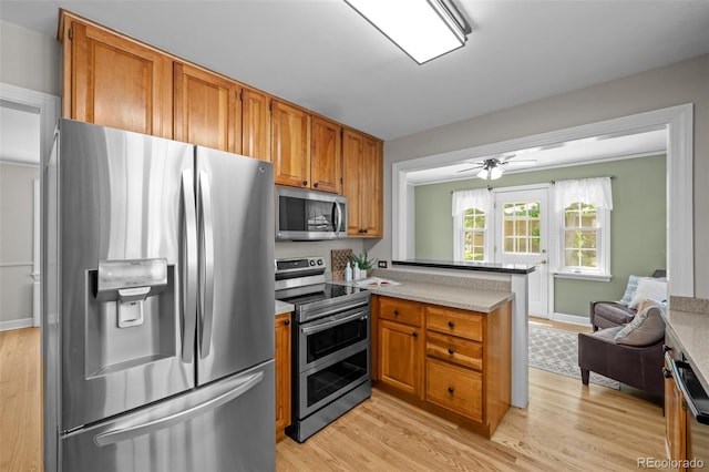 1033 Estes St, Lakewood, CO 80215 - kitchen with appliances with stainless steel finishes, a peninsula, light wood-type flooring, brown cabinets, and light countertops