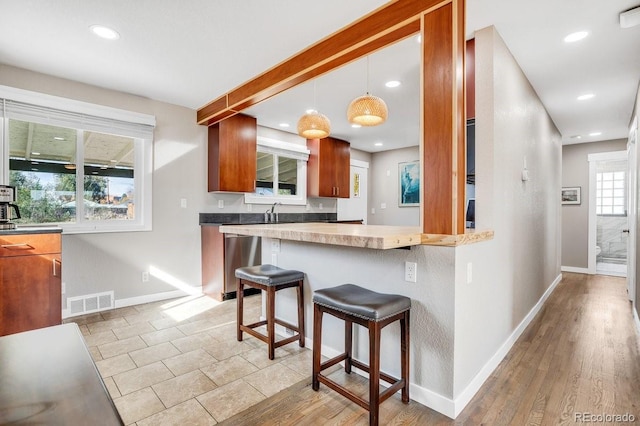 kitchen featuring kitchen peninsula, a breakfast bar, light wood-type flooring, pendant lighting, and sink