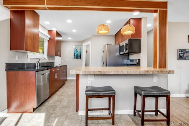 kitchen with a breakfast bar area, kitchen peninsula, sink, pendant lighting, and appliances with stainless steel finishes