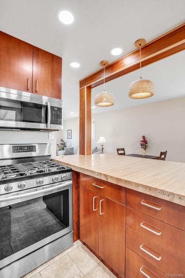 kitchen featuring kitchen peninsula, appliances with stainless steel finishes, pendant lighting, light tile patterned floors, and butcher block countertops