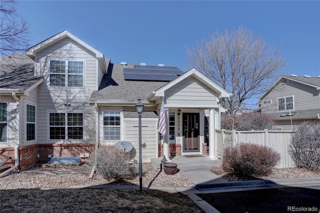 view of front facade with solar panels, fence, brick siding, and roof with shingles