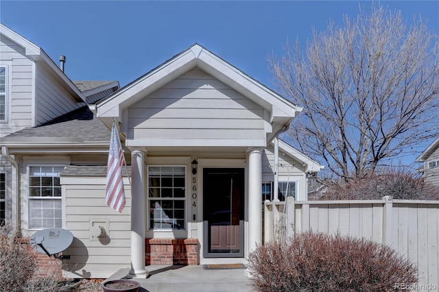 view of exterior entry featuring a shingled roof and fence