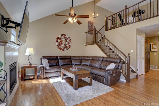 living room with visible vents, high vaulted ceiling, light wood-style flooring, a fireplace, and stairs