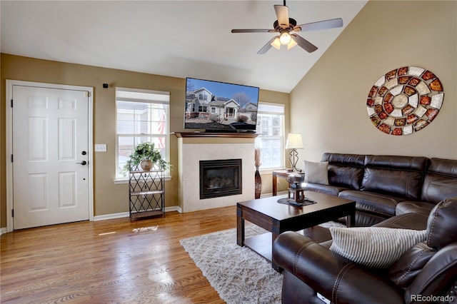 living room featuring lofted ceiling, a ceiling fan, a tiled fireplace, wood finished floors, and baseboards