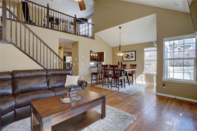 living room with stairway, wood finished floors, high vaulted ceiling, and ceiling fan