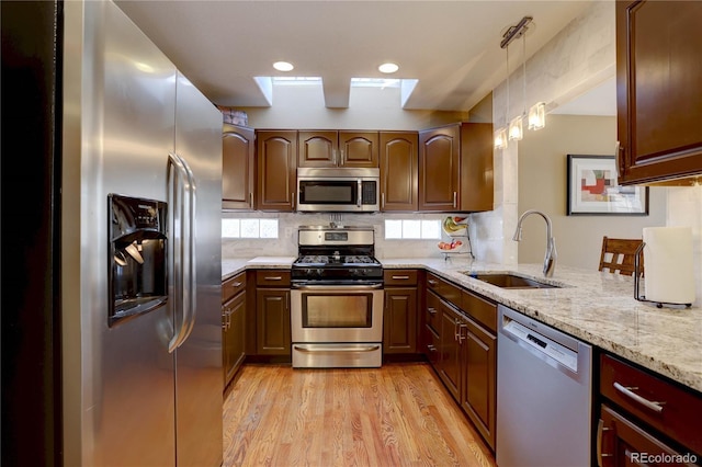 kitchen with light wood-type flooring, a sink, light stone counters, tasteful backsplash, and stainless steel appliances