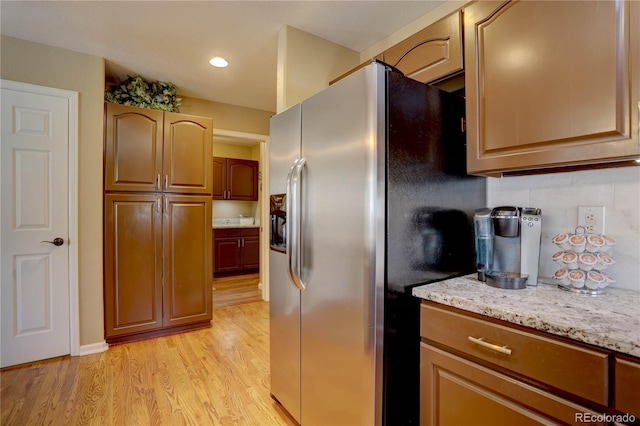 kitchen with light stone counters, decorative backsplash, stainless steel fridge, and light wood-style floors