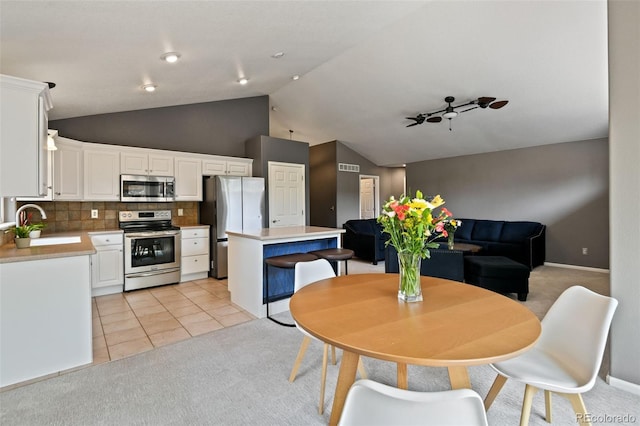 8829 S Dudley St, Littleton, CO 80128 - kitchen with stainless steel appliances, vaulted ceiling, light colored carpet, white cabinets, and a kitchen island