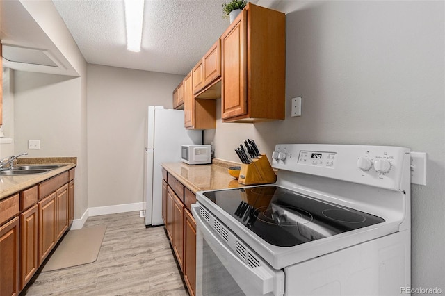 kitchen featuring white appliances, a sink, light wood-type flooring, a textured ceiling, and brown cabinetry