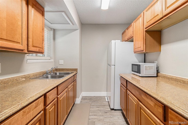 kitchen with white appliances, a sink, light wood finished floors, a textured ceiling, and light countertops