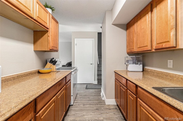 kitchen with electric range, light wood-style floors, brown cabinetry, and a sink