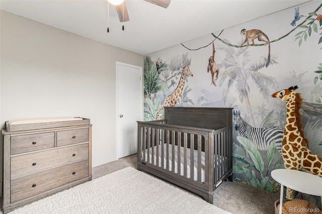carpeted bedroom featuring a nursery area and ceiling fan