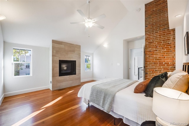 bedroom featuring high vaulted ceiling, hardwood / wood-style flooring, a tile fireplace, and ceiling fan