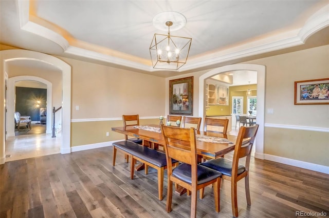 dining area with baseboards, a raised ceiling, arched walkways, an inviting chandelier, and dark wood-type flooring