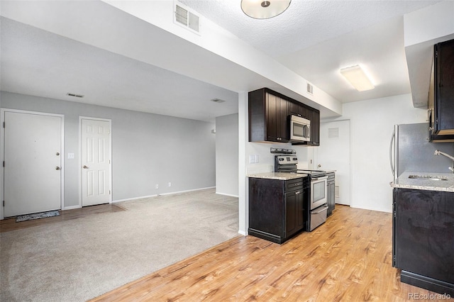 kitchen featuring sink, light colored carpet, a textured ceiling, dark brown cabinets, and appliances with stainless steel finishes